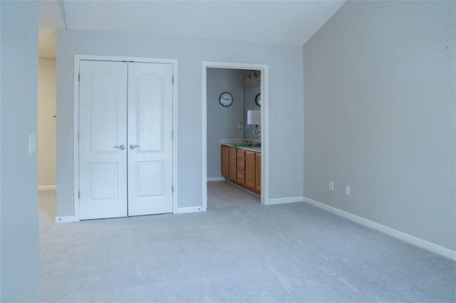 unfurnished bedroom featuring ensuite bathroom, light colored carpet, and a closet