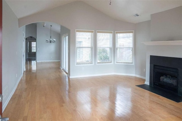 unfurnished living room featuring lofted ceiling, a wealth of natural light, light hardwood / wood-style floors, and a chandelier