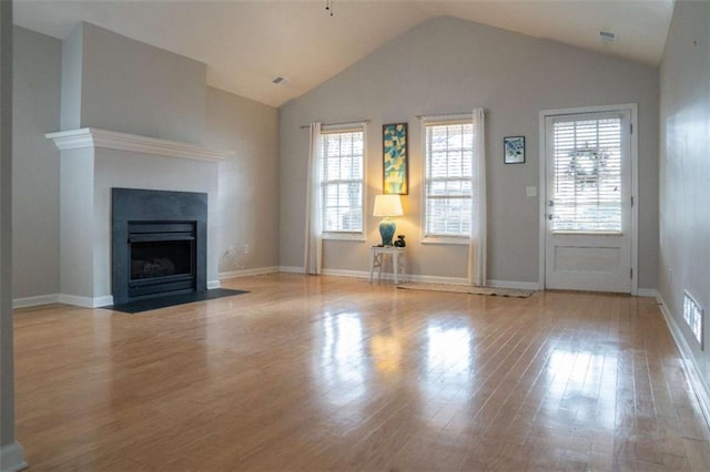 unfurnished living room with vaulted ceiling, a healthy amount of sunlight, and light hardwood / wood-style floors