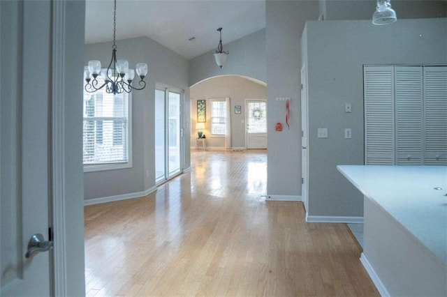 unfurnished dining area featuring high vaulted ceiling, a chandelier, and light hardwood / wood-style floors