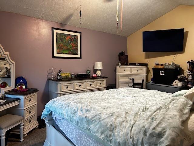 bedroom with a textured ceiling, dark carpet, and lofted ceiling