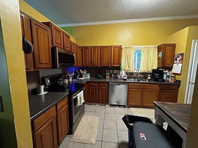 kitchen featuring sink, appliances with stainless steel finishes, a textured ceiling, light tile patterned floors, and ornamental molding