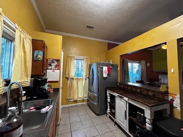 kitchen featuring sink, crown molding, stainless steel fridge, light tile patterned floors, and a textured ceiling