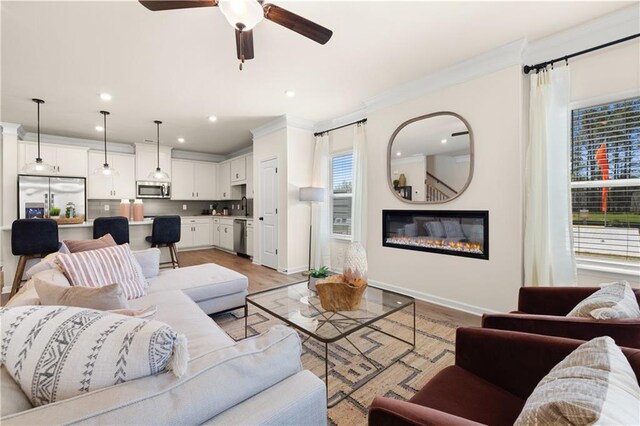 living room with light wood-type flooring, ceiling fan, and crown molding