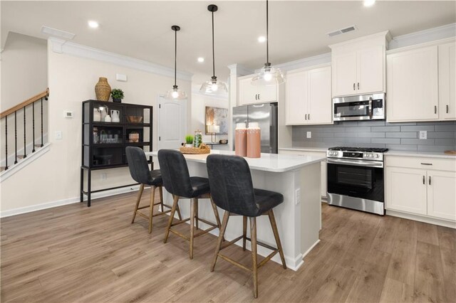 kitchen featuring stainless steel appliances, a kitchen island, white cabinetry, hanging light fixtures, and hardwood / wood-style flooring