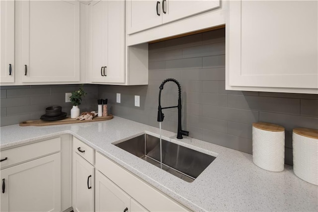 kitchen with tasteful backsplash, white cabinetry, sink, and light stone countertops