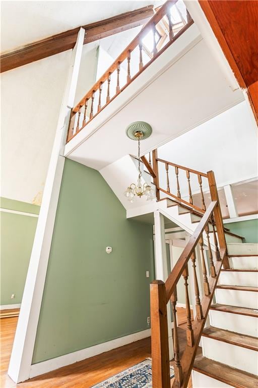 stairway featuring wood-type flooring, lofted ceiling, and a notable chandelier