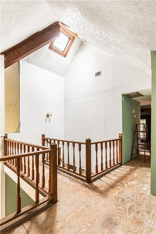 additional living space with hardwood / wood-style floors, a textured ceiling, and vaulted ceiling with skylight