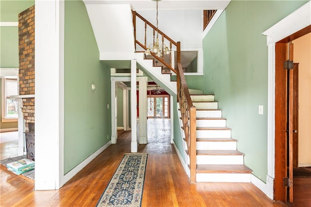 stairway with a towering ceiling, hardwood / wood-style flooring, and a brick fireplace