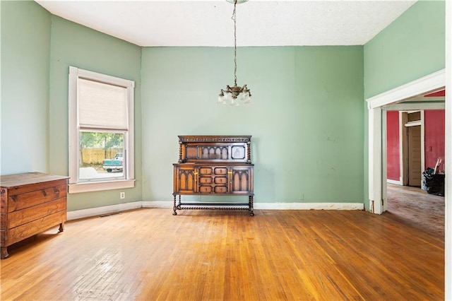 empty room with wood-type flooring and an inviting chandelier