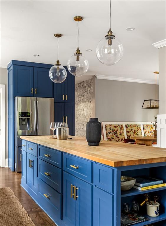 bar featuring crown molding, hanging light fixtures, stainless steel fridge, and dark wood-style flooring