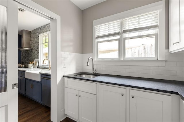 kitchen with white cabinetry, wall chimney range hood, dark countertops, and a sink