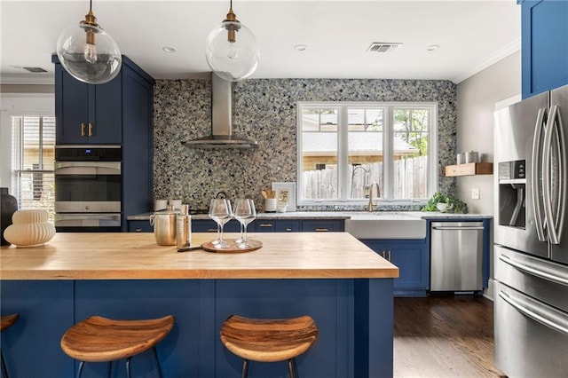 kitchen featuring butcher block countertops, stainless steel appliances, visible vents, wall chimney exhaust hood, and blue cabinetry
