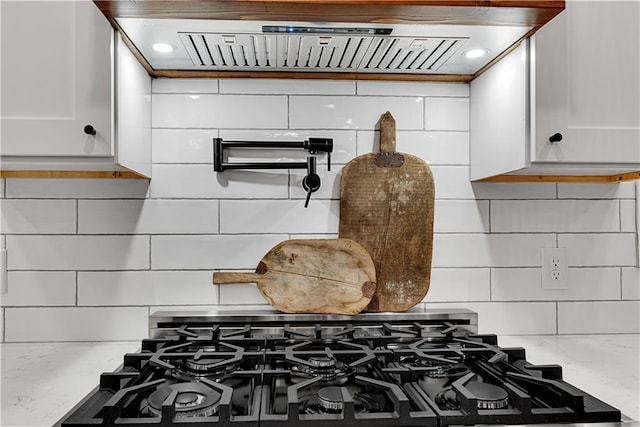 interior details with black range with gas stovetop, white cabinetry, backsplash, and exhaust hood