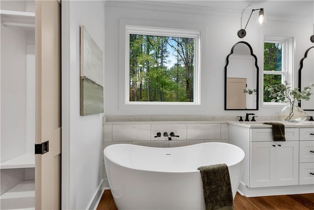 bathroom with ornamental molding, a tub to relax in, vanity, and wood-type flooring