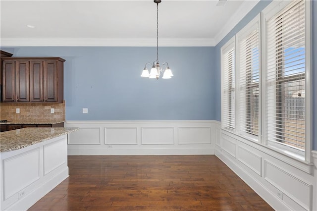 unfurnished dining area with dark wood-type flooring, a chandelier, wainscoting, and ornamental molding