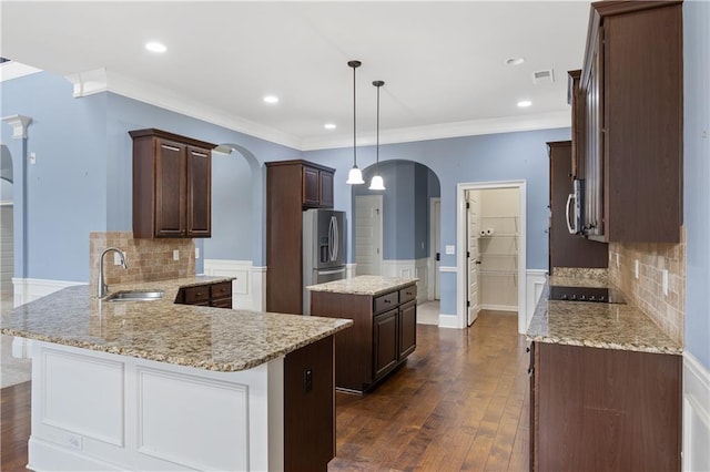 kitchen featuring a center island, appliances with stainless steel finishes, a peninsula, arched walkways, and a sink