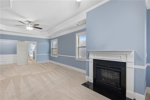 unfurnished living room featuring carpet, a fireplace with flush hearth, ornamental molding, a raised ceiling, and a ceiling fan