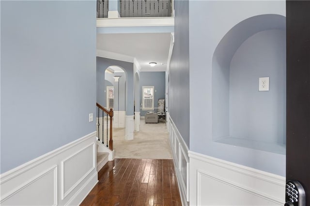 hallway featuring arched walkways, a decorative wall, stairs, and hardwood / wood-style floors