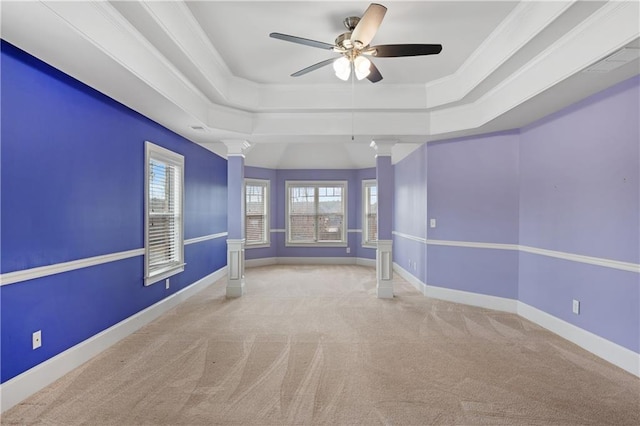 carpeted empty room with a raised ceiling, decorative columns, crown molding, and baseboards