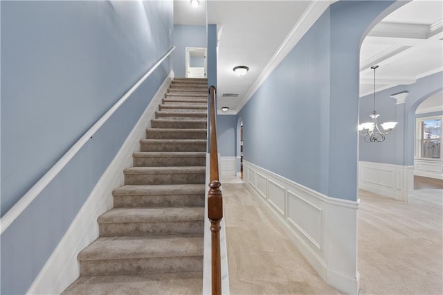 stairway with arched walkways, carpet, crown molding, and a decorative wall