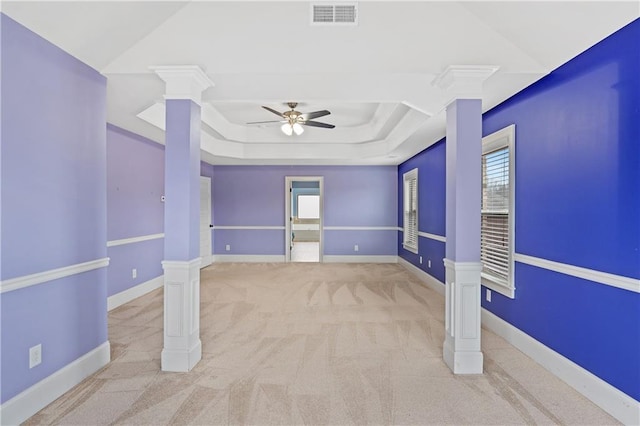 carpeted spare room with visible vents, a ceiling fan, a tray ceiling, baseboards, and ornate columns