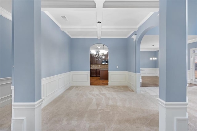 unfurnished dining area featuring carpet, visible vents, coffered ceiling, an inviting chandelier, and arched walkways