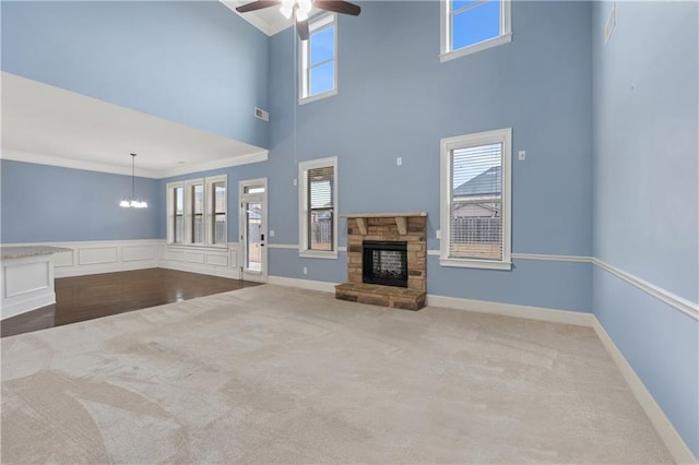 unfurnished living room featuring visible vents, carpet floors, a fireplace, ornamental molding, and ceiling fan with notable chandelier