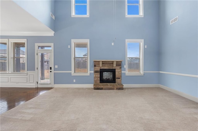 unfurnished living room featuring a stone fireplace, carpet, visible vents, and a wealth of natural light