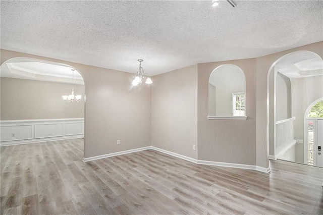 empty room with an inviting chandelier, a textured ceiling, and wood finished floors