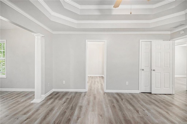 spare room featuring crown molding, baseboards, wood finished floors, ornate columns, and a tray ceiling