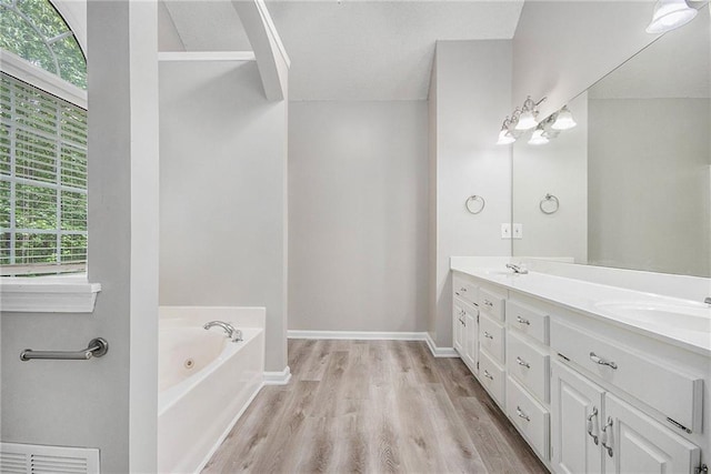bathroom featuring double vanity, a bath, visible vents, wood finished floors, and a sink