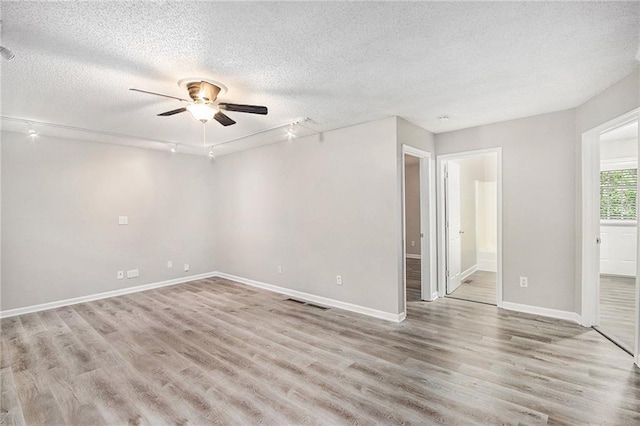 empty room featuring ceiling fan, a textured ceiling, rail lighting, baseboards, and light wood-type flooring