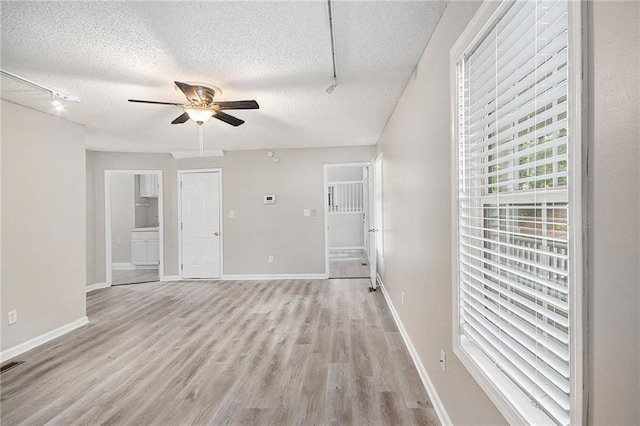 spare room featuring ceiling fan, a textured ceiling, rail lighting, baseboards, and light wood-style floors
