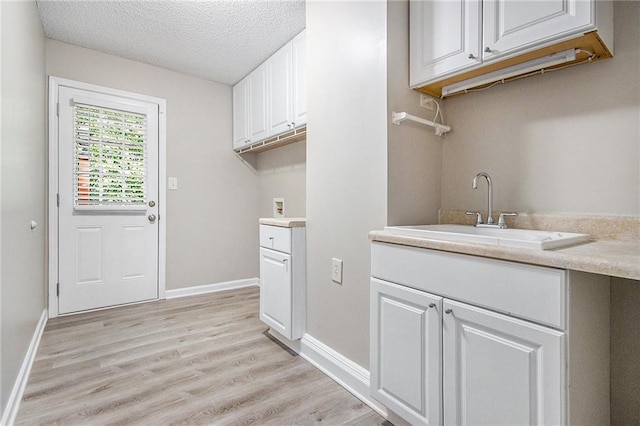 clothes washing area featuring baseboards, light wood-type flooring, a textured ceiling, a sink, and washer hookup