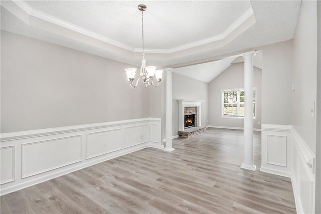 unfurnished dining area featuring a textured ceiling, a chandelier, a stone fireplace, light wood-style flooring, and a tray ceiling