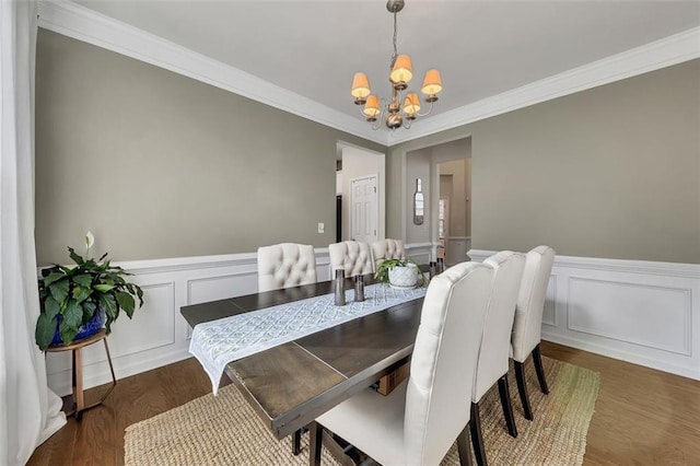 dining space featuring dark wood-style floors, ornamental molding, a wainscoted wall, and a notable chandelier