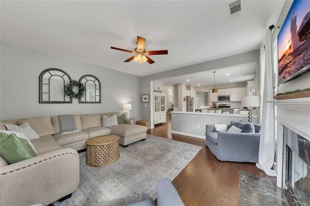 living room with dark wood-style flooring, a fireplace, visible vents, ceiling fan, and baseboards