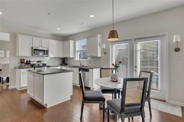 kitchen featuring stainless steel appliances, visible vents, white cabinetry, hanging light fixtures, and dark countertops