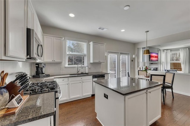 kitchen featuring a kitchen island, a sink, white cabinetry, appliances with stainless steel finishes, and decorative light fixtures