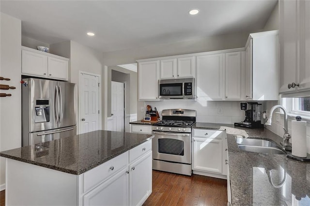 kitchen featuring a sink, a kitchen island, white cabinets, appliances with stainless steel finishes, and dark stone countertops