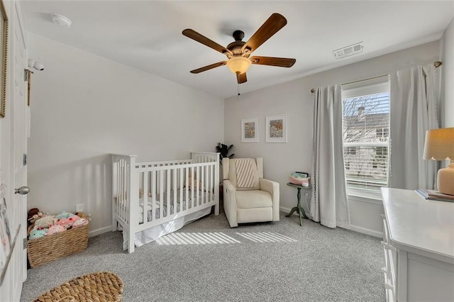 bedroom featuring a nursery area, baseboards, visible vents, and light colored carpet