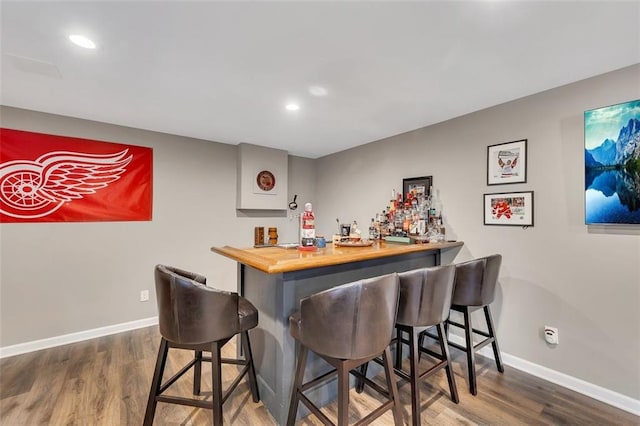 bar with a bar, baseboards, dark wood finished floors, and recessed lighting