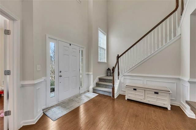 foyer entrance featuring a decorative wall, stairway, a towering ceiling, and wood finished floors