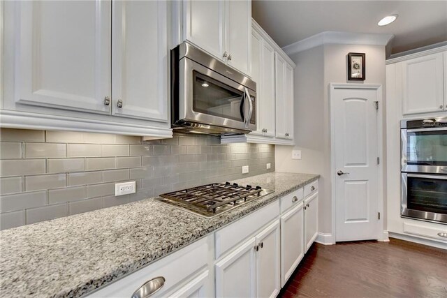 kitchen featuring dark wood-type flooring, stainless steel appliances, backsplash, light stone countertops, and white cabinetry