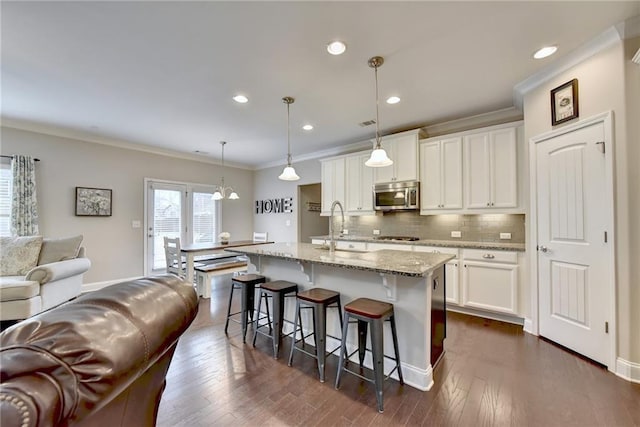 kitchen with appliances with stainless steel finishes, an island with sink, white cabinetry, decorative light fixtures, and dark hardwood / wood-style floors