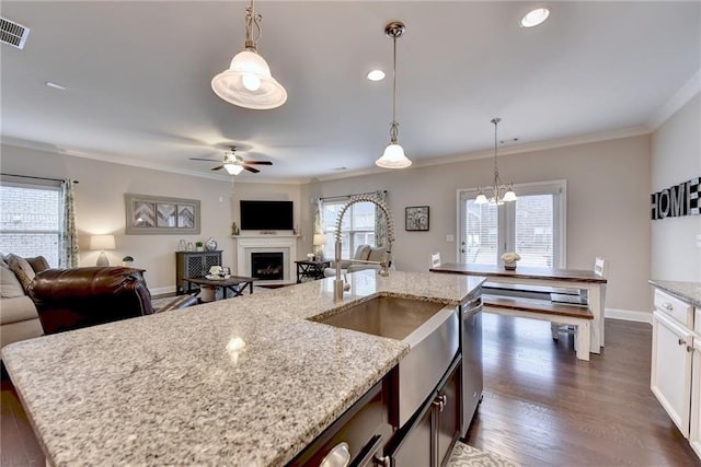 kitchen with dark hardwood / wood-style flooring, a kitchen island with sink, light stone counters, and pendant lighting