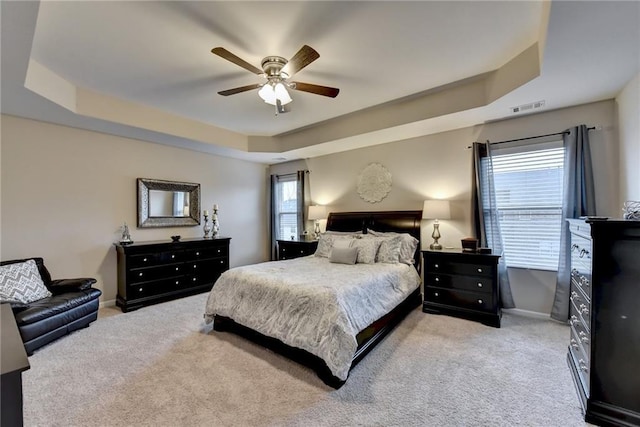 carpeted bedroom featuring a tray ceiling and ceiling fan