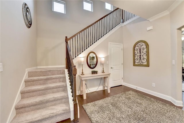 staircase featuring hardwood / wood-style floors, crown molding, and a towering ceiling