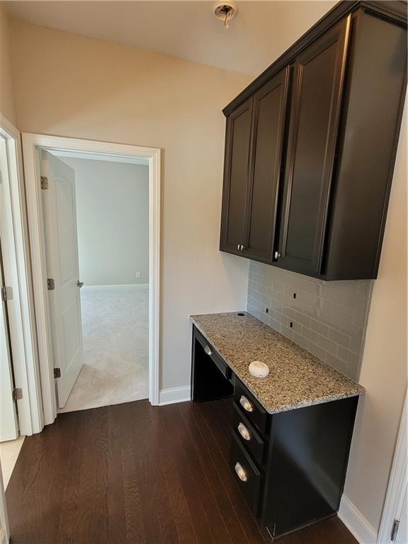 kitchen with dark brown cabinets, decorative backsplash, light stone counters, and dark wood-type flooring